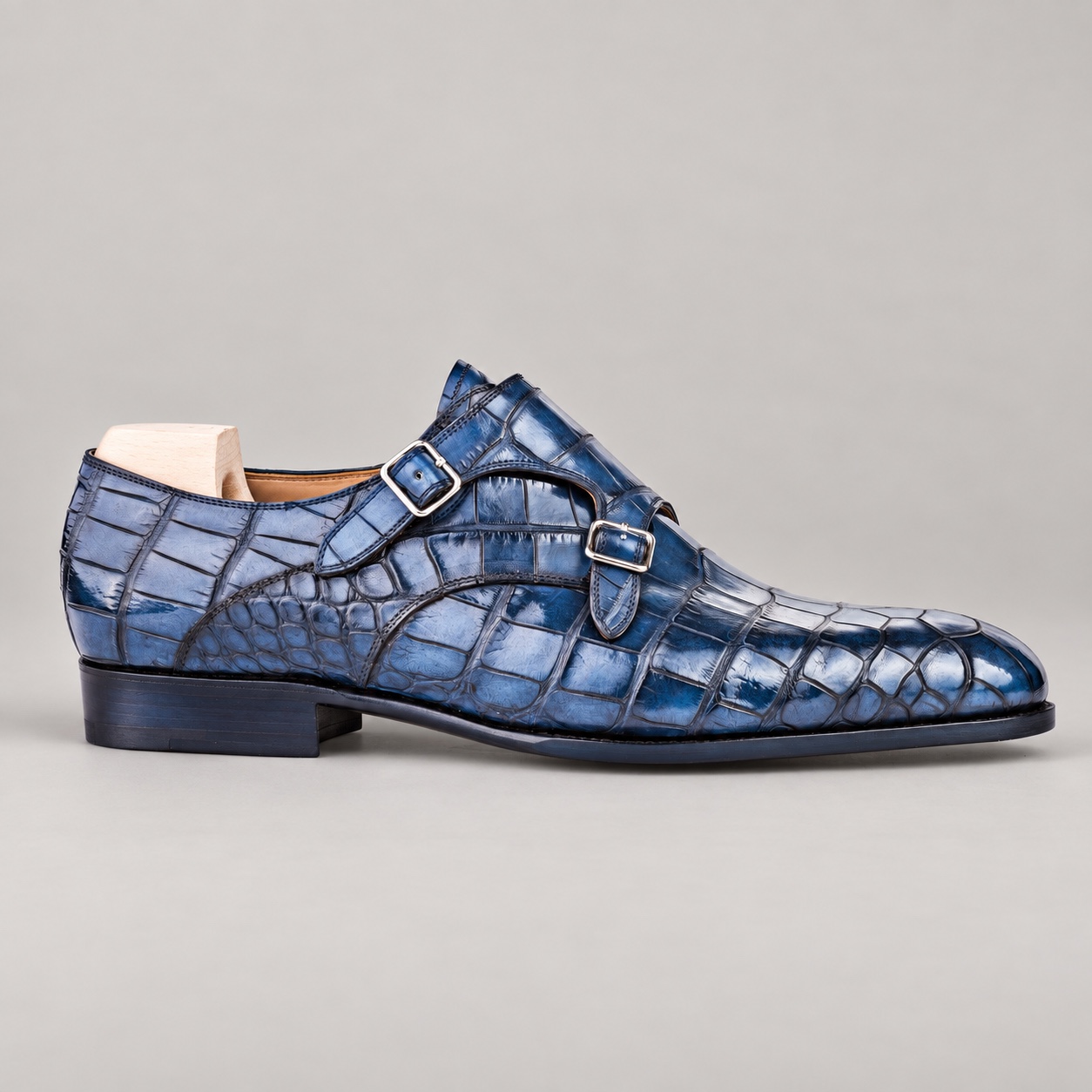 Side profile of a blue alligator double monk strap shoe with two silver buckles