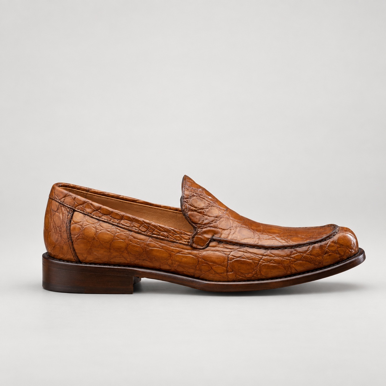 Side profile of a mahogany alligator loafer with a low heel and brown patina sole edge