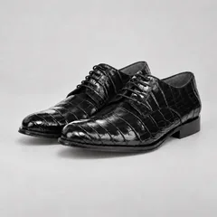 Pair of polished black alligator lace-up shoes with dark grey cow suede lining on a warm-grey background