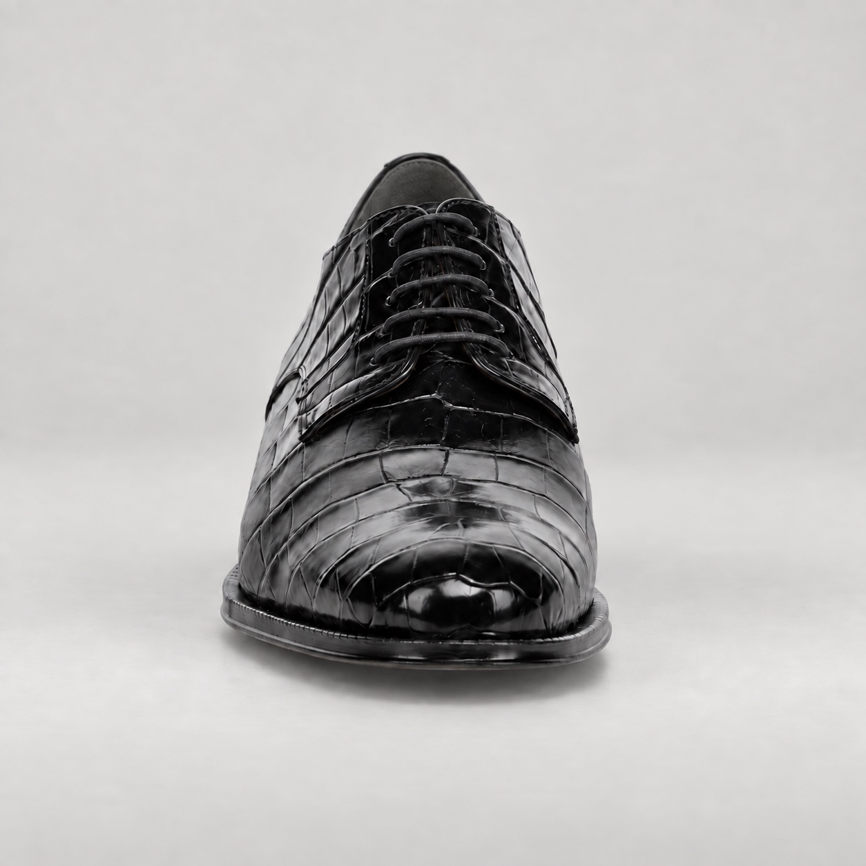 Front view of a polished black alligator lace-up shoe with a gently tapered toe