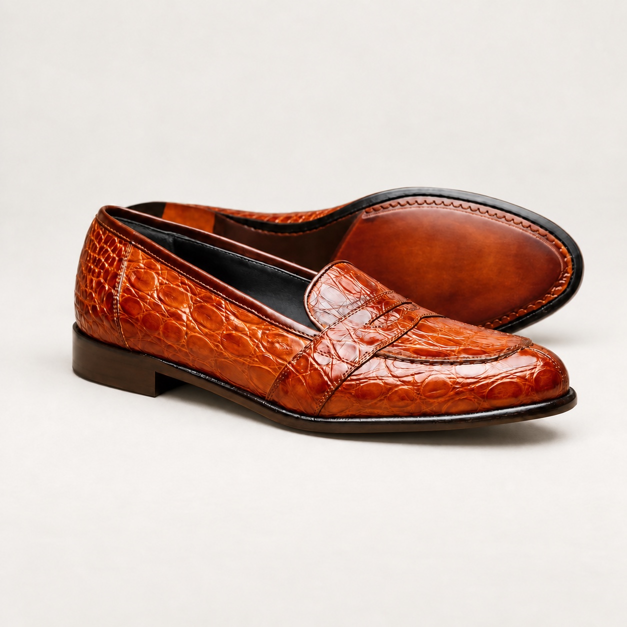Cognac crocodile penny loafers on a warm-grey studio background
