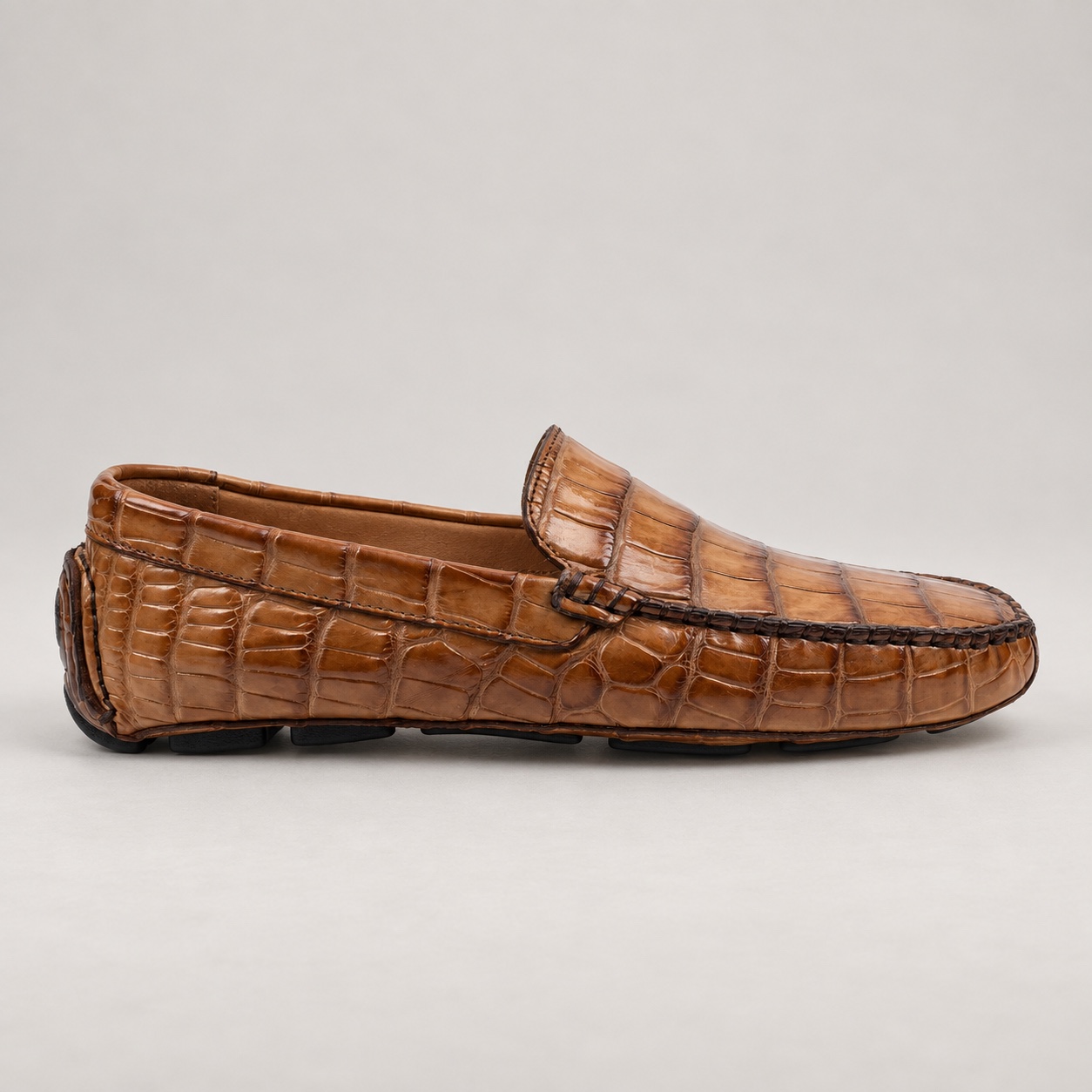 Side profile of a tan crocodile driving loafer with a low silhouette and segmented sole